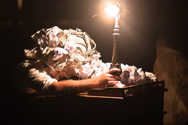 Photo of a head buried in crumpled paper lit by a bare lightbulb