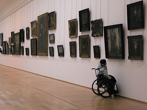 person in a wheelchair reading label on wall in gallery 