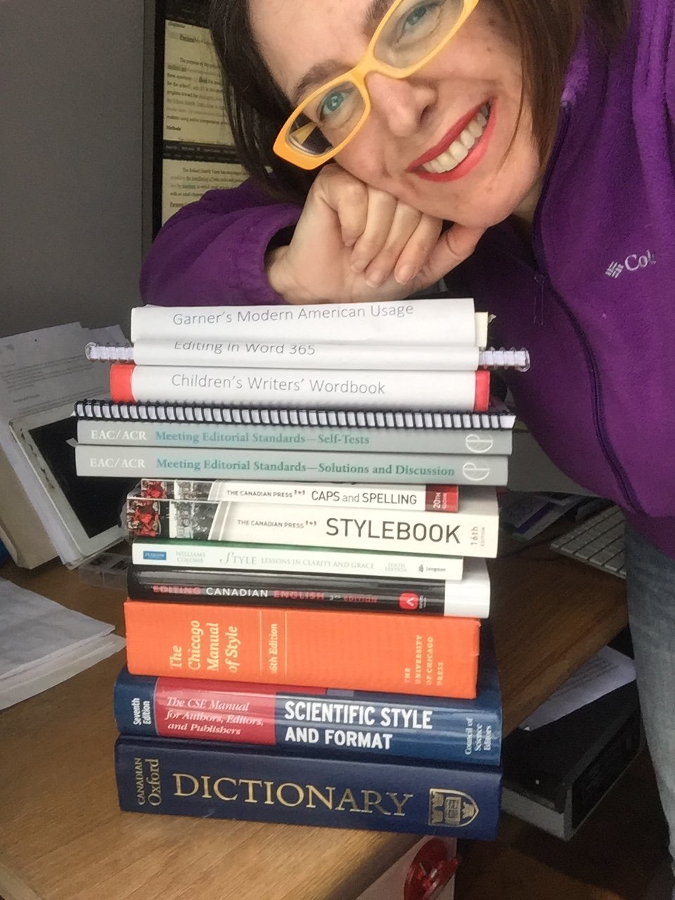 Selfie with pile of books I refer to just about daily for editing: Modern American Usage, Chicago Manual of Style, Scientific Style and format, Canadian Oxford Dictionary, Canadian Press Style plus their Caps and Spelling, Meeting Professional Editorial Standards (now Edit like a pro), Children's writers word book, Editing in Word 365