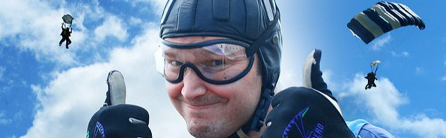 parachutist giving two thumbs up with parachuters landing in background