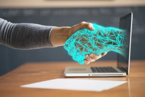 closeup on handshake between human and an imagined AI hand in the form of glowing geometric outline reaching out from a laptop screen